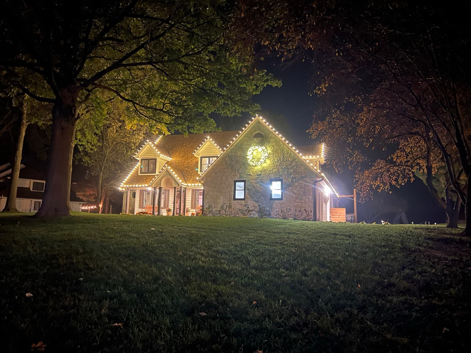 Warm white Christmas lights on stone cottage with lit trees in Kansas City