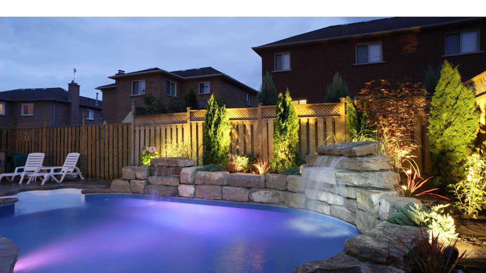 Backyard pool with waterfall and stone wall accent lighting at night