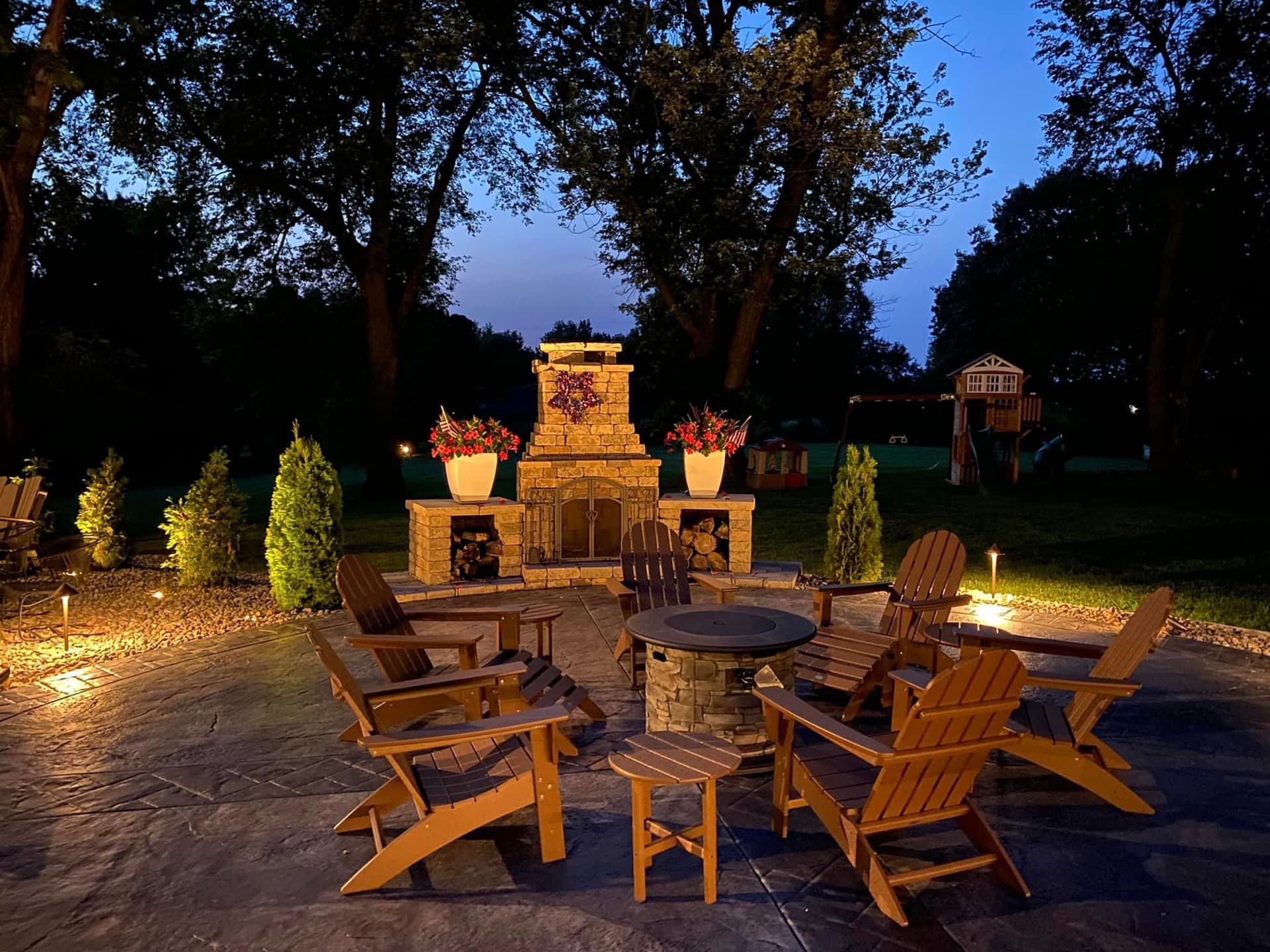 Stone patio with fireplace and Adirondack chairs illuminated at night